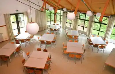 Bright dining hall with tables and large windows in the main house of Sporthostel Schubybeach