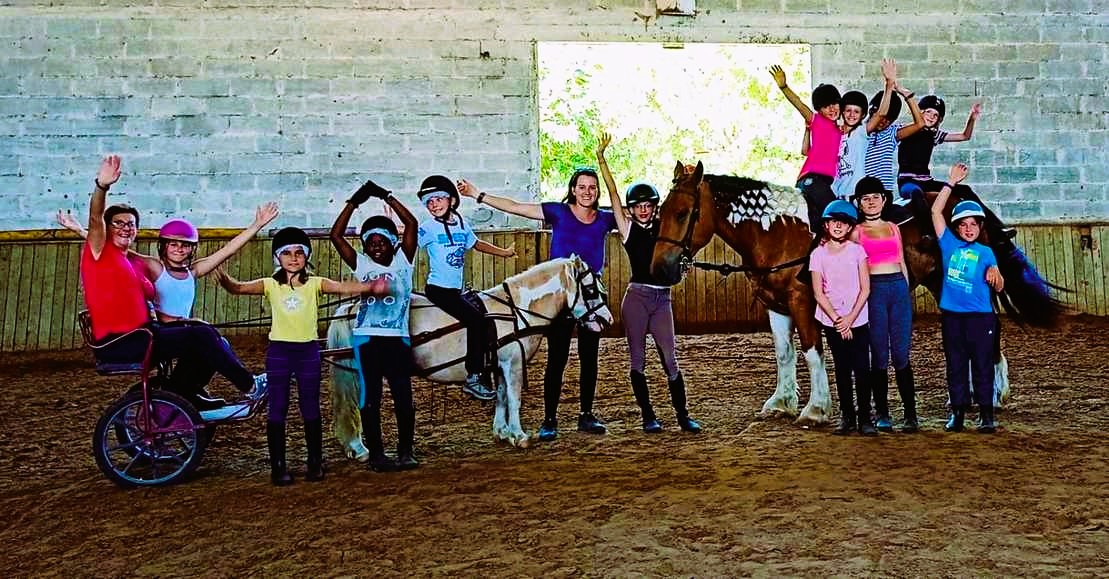 A group of children and leaders raising their arms beside a horse in the riding arena at Domaine de Lauzerte