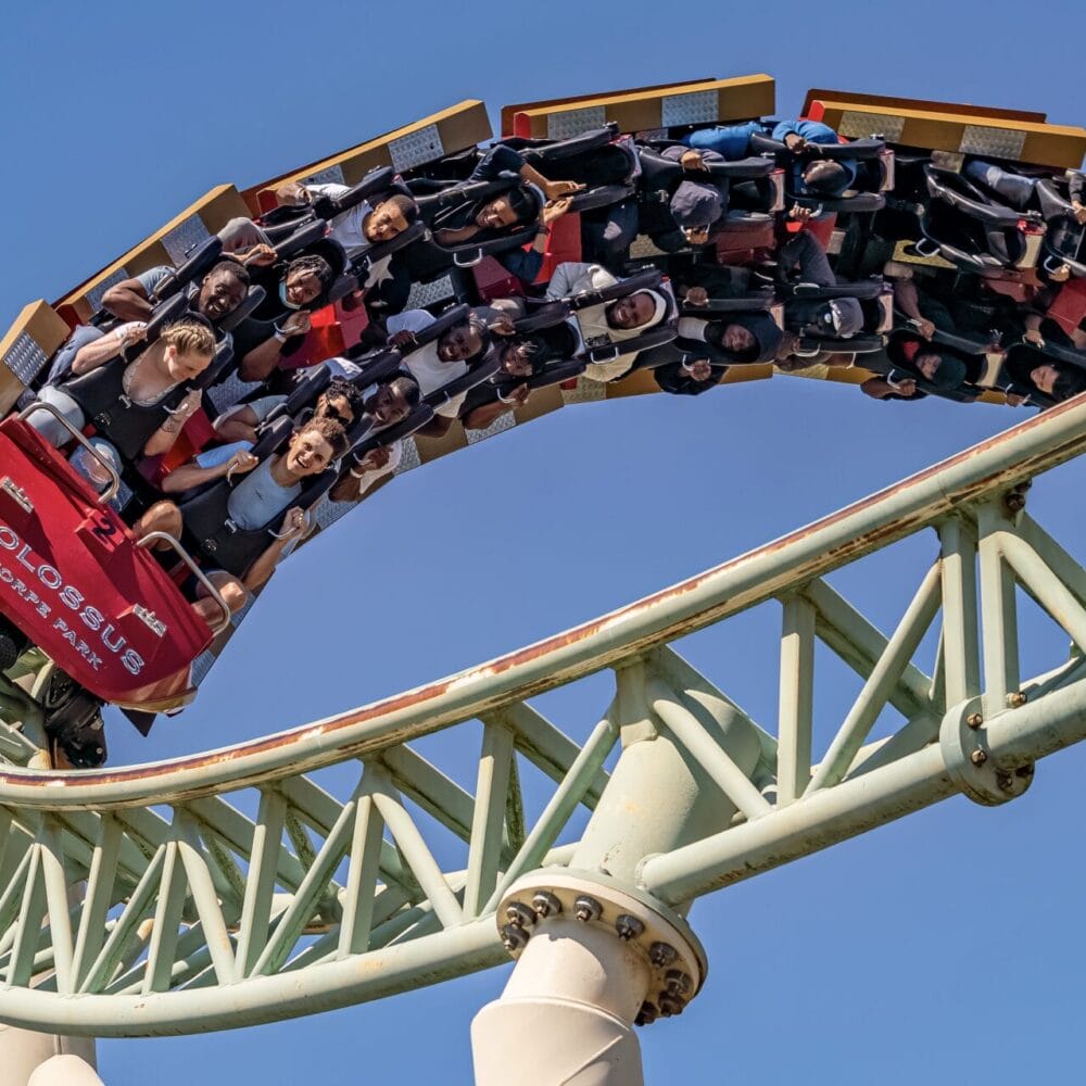 A rollercoaster train full of riders curving against a clear blue sky at a theme park, an excursion destination