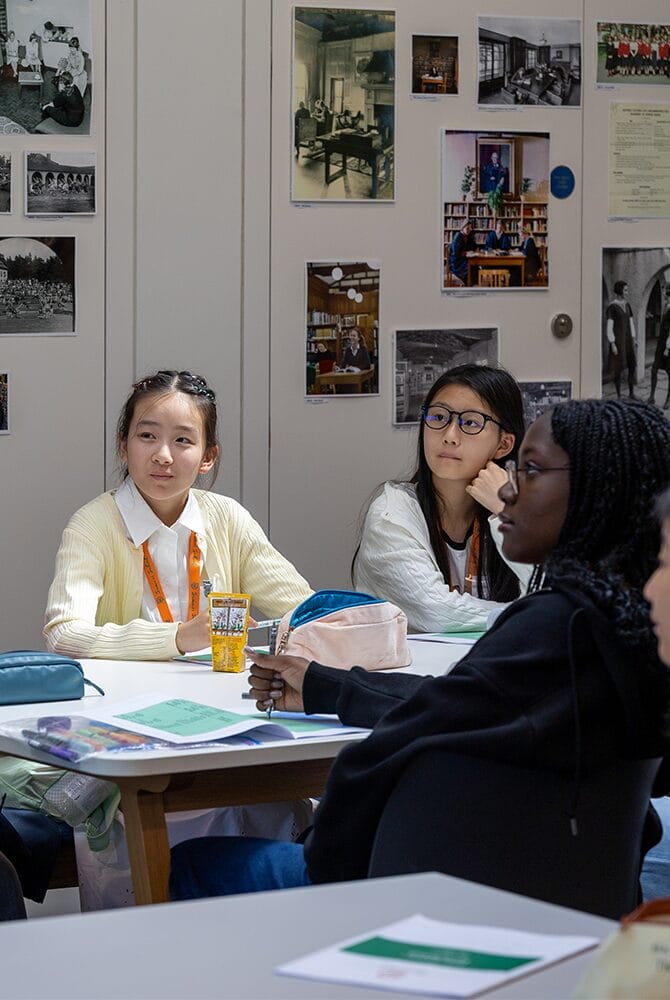 Summer school students listening at their desks in a classroom with photographs pinned to the wall
