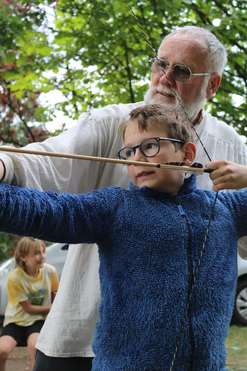 An instructor steadying a boy as he draws a bow at the archery range, Beginner Weeks camp in Vallendar