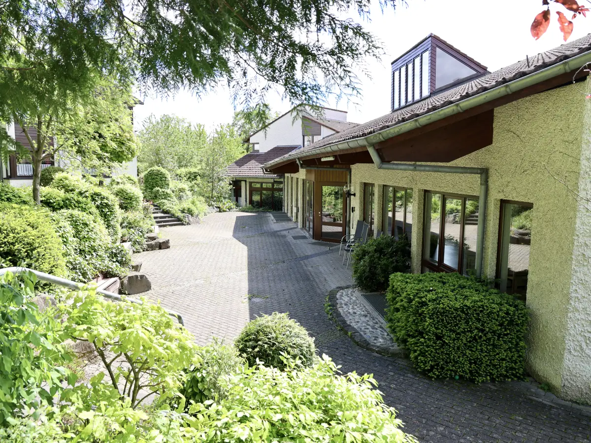 The low guest house of the Ferienanlage Marienberg seen from the drive, with shrubs and lawn in front