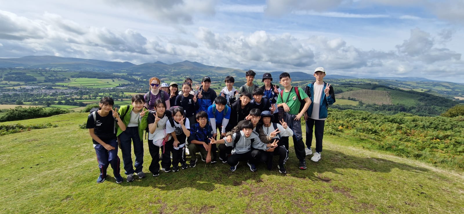 Group of campers and staff posing on a grassy hilltop with views over the Brecon Beacons