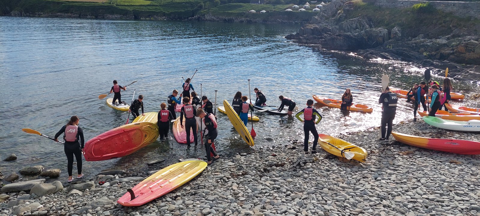 Stand-up paddleboards and kayaks being launched from the stony shore