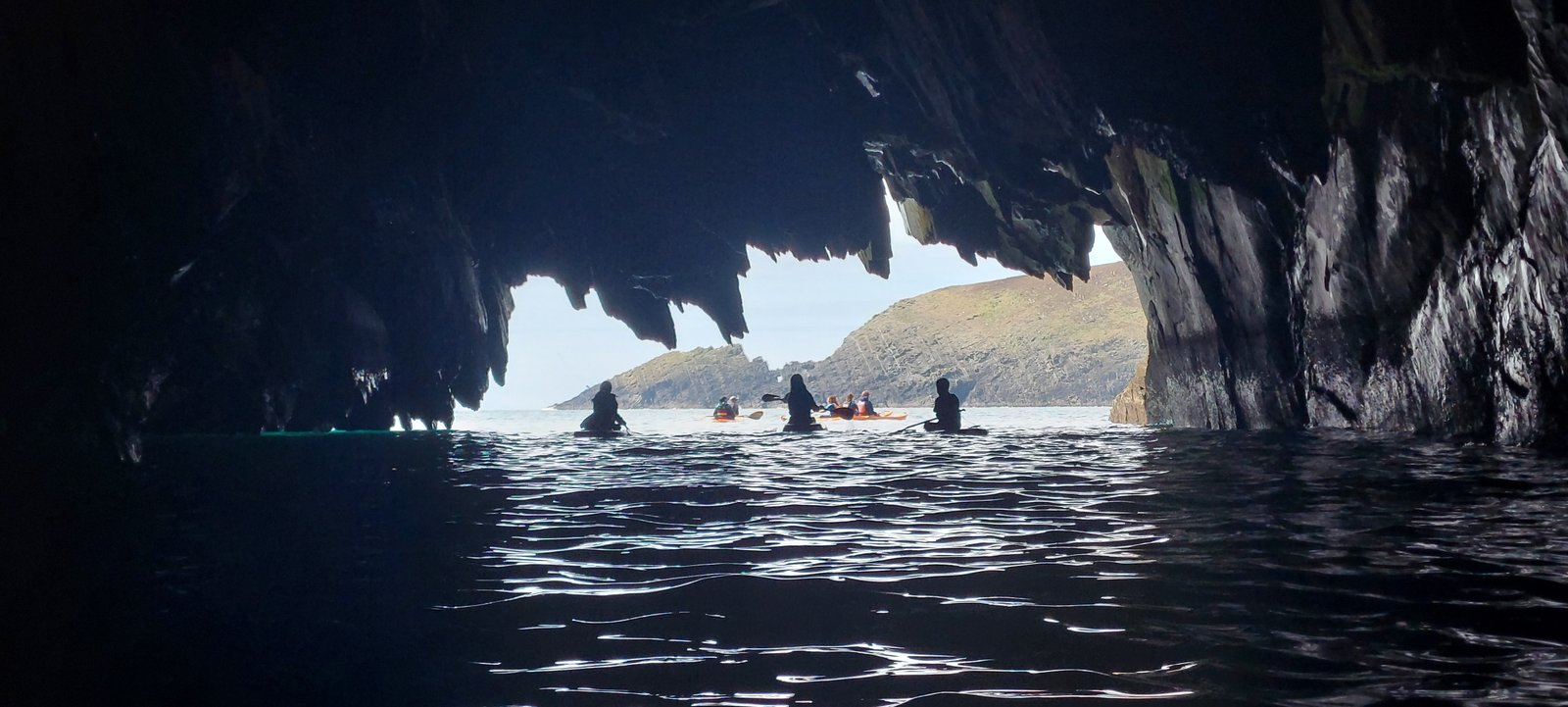 View from inside a sea cave towards kayakers on the water outside