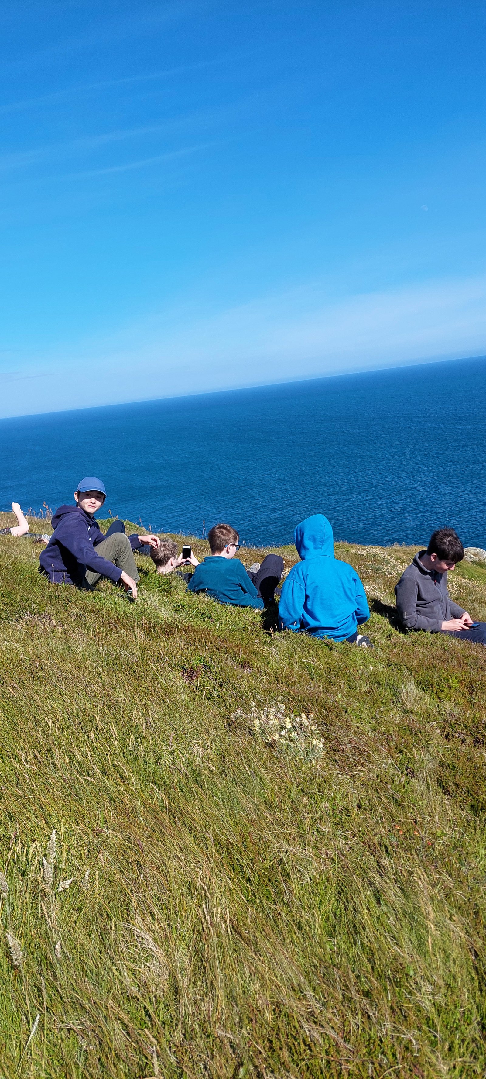 Participants sitting on the clifftop grass above the sea