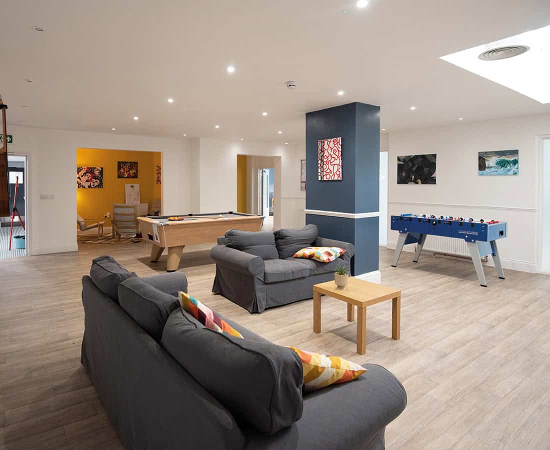 A student common room with grey sofas, a pool table and a table football game