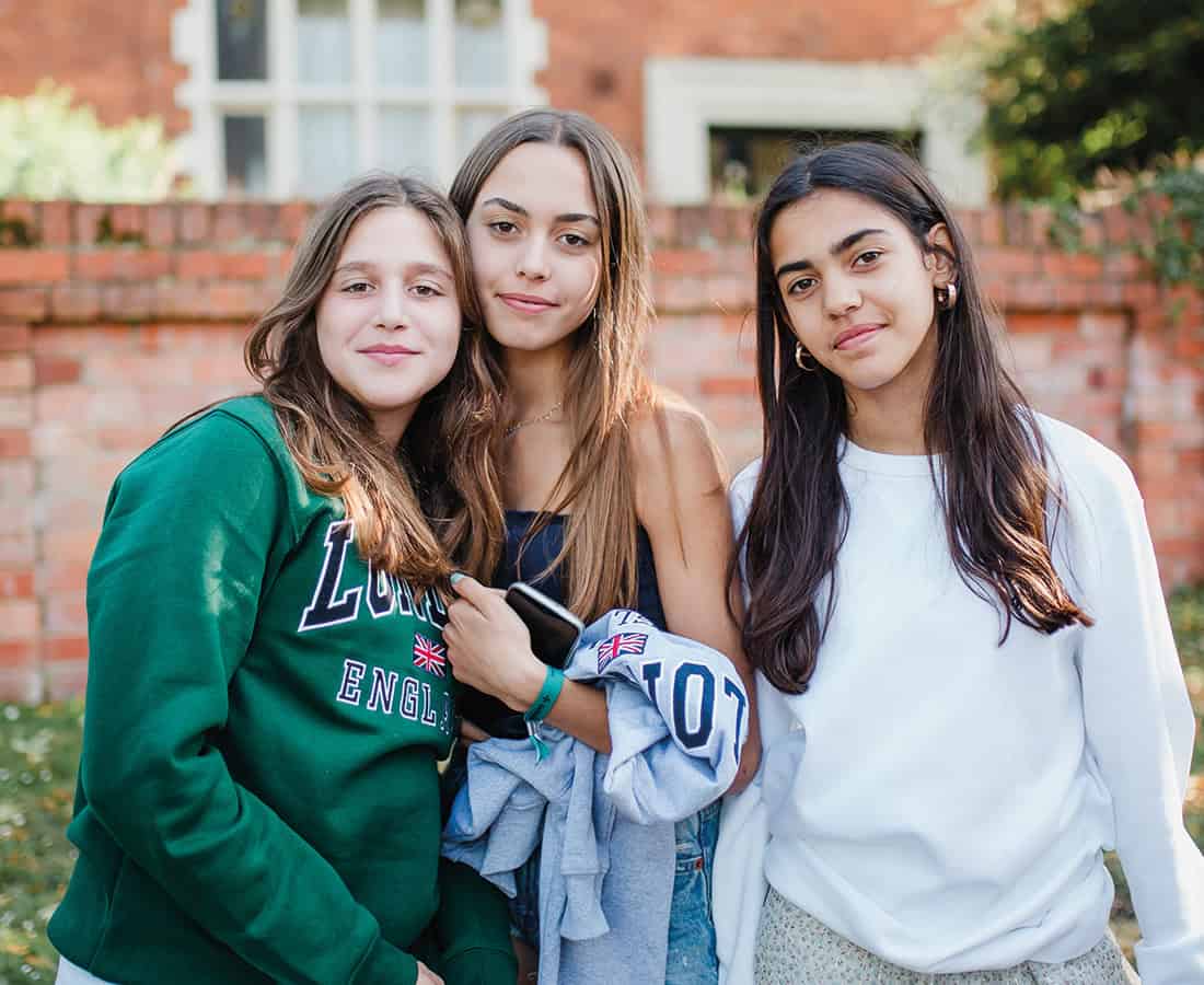 Three students stand together and smile outside a red brick building on campus