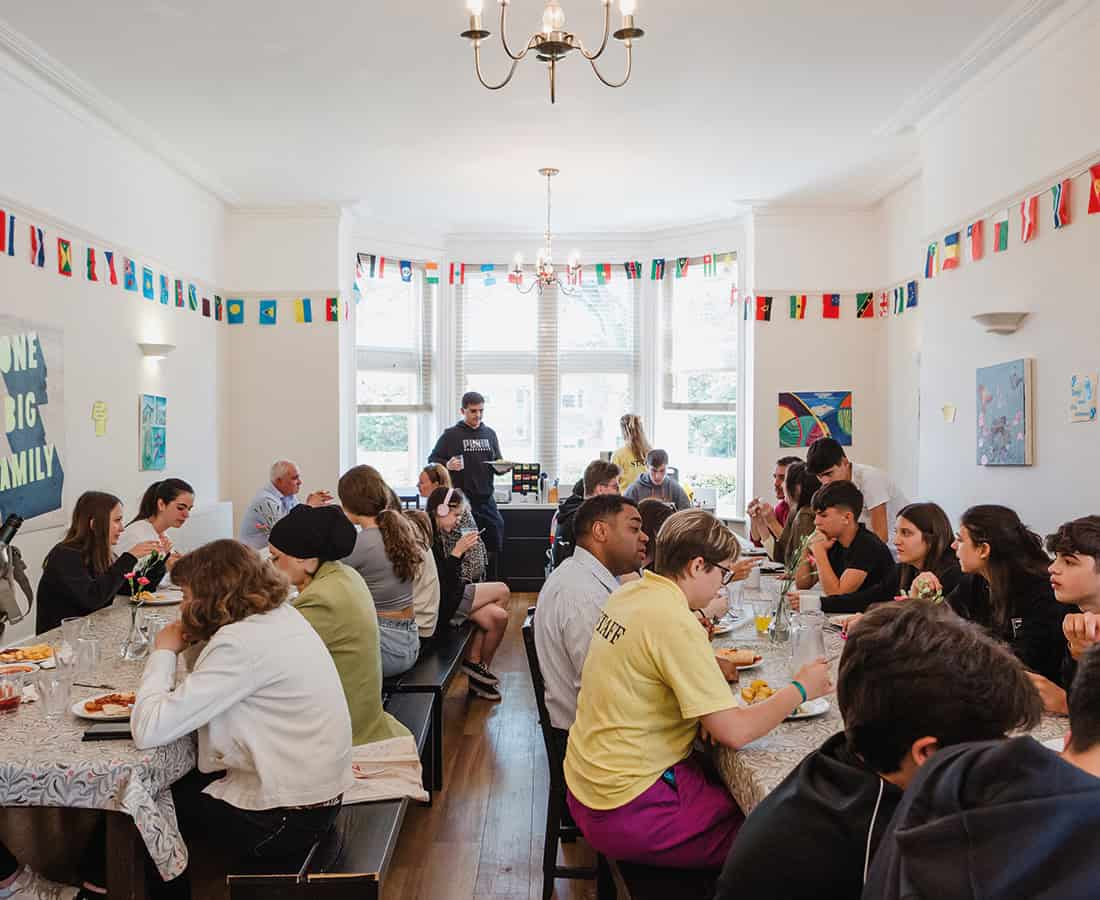 Students eat a meal at long tables in a dining hall hung with bunting