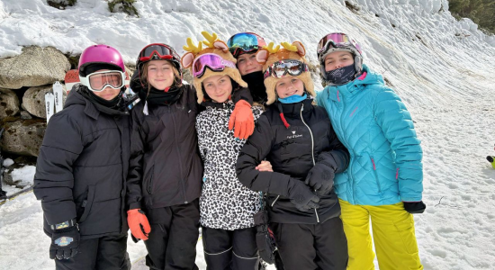 Six young skiers in helmets and goggles standing arm in arm in the snow