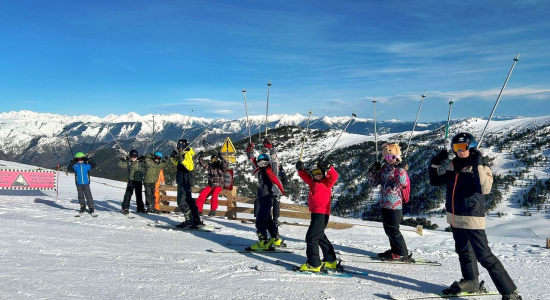 Young skiers in bright jackets waving from the piste with the valley behind them