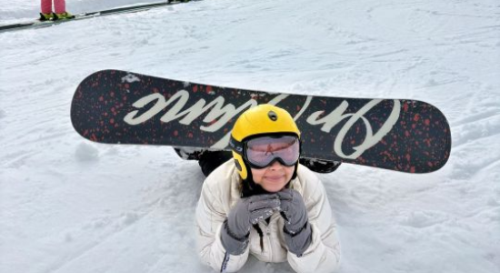 A young snowboarder in goggles holding her board upright in the snow
