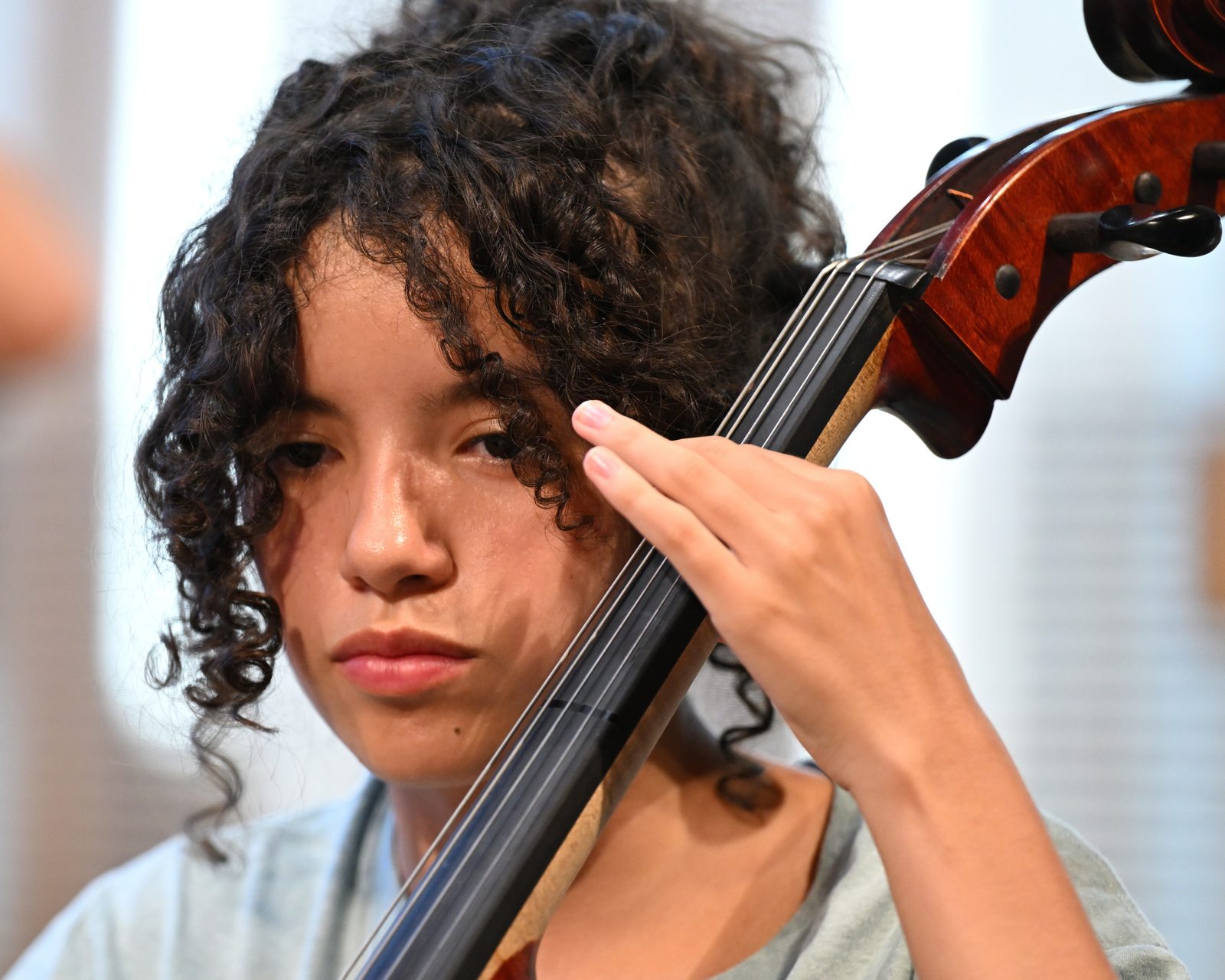 Close-up of a student playing a cello, the bow drawn across the strings beside their face.