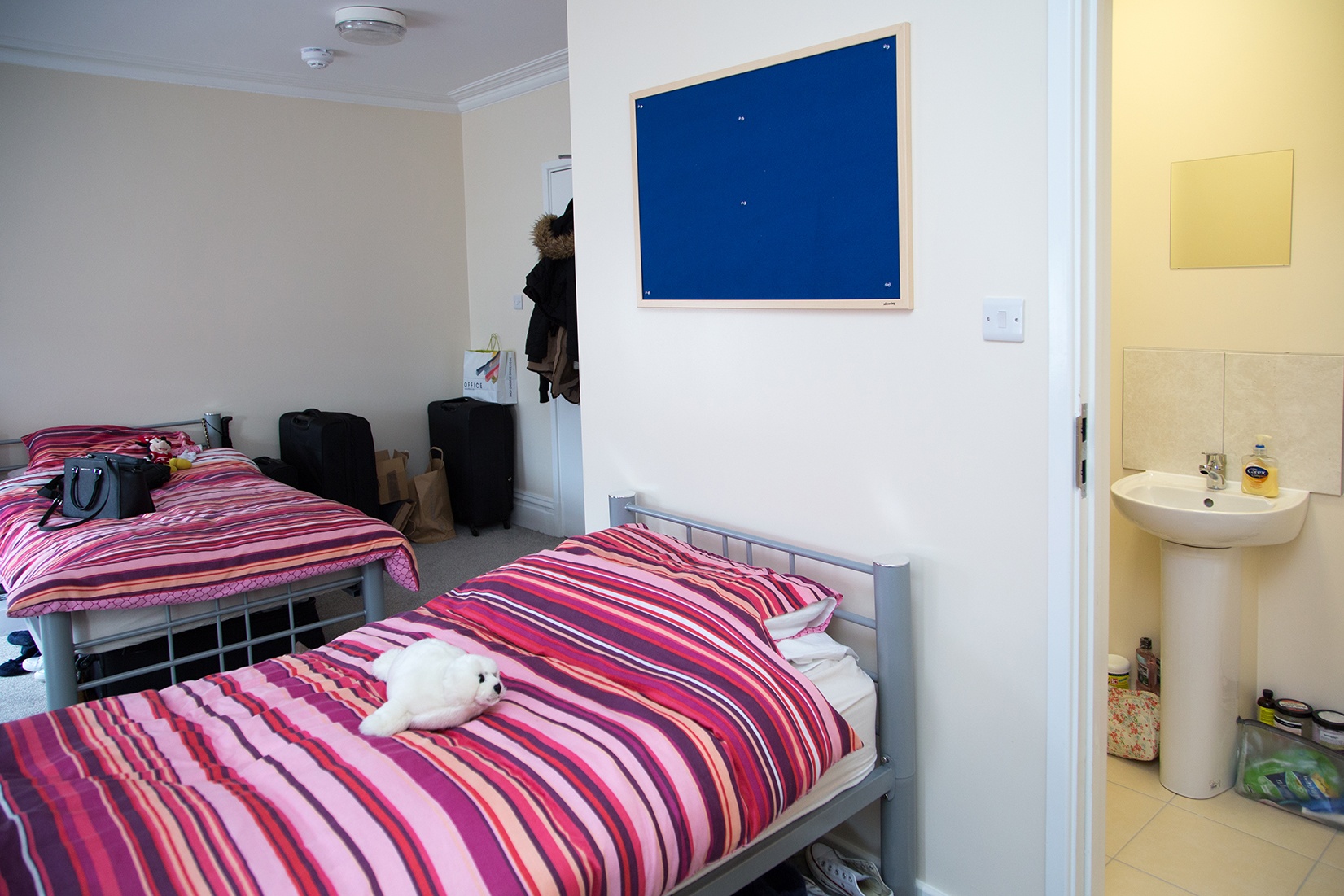 Bedroom in a Select English residence with a striped bedspread, washbasin and noticeboard