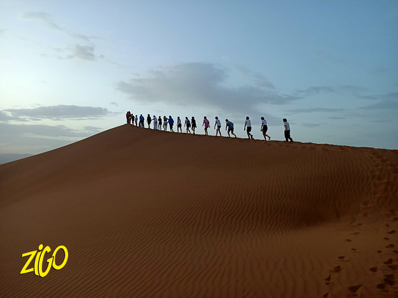 A single file of young people walking along the crest of a sand dune in the Moroccan desert