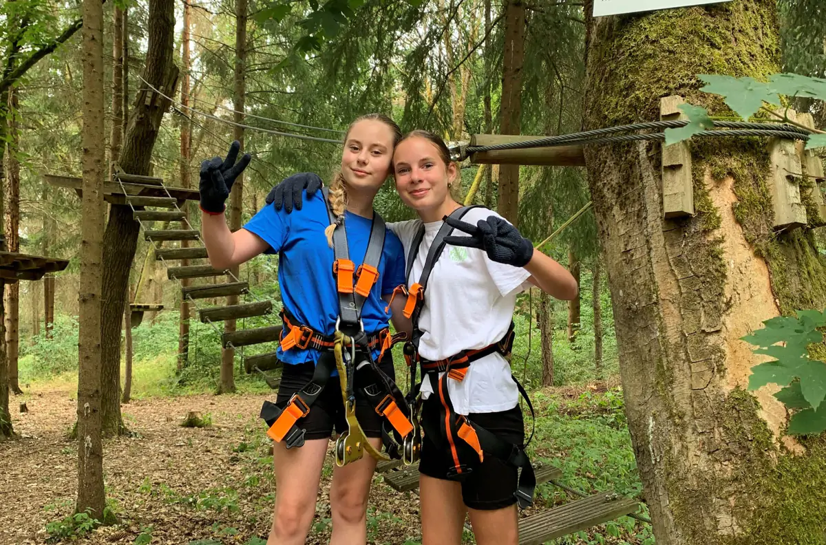 Two girls in climbing harnesses on a platform in the climbing forest