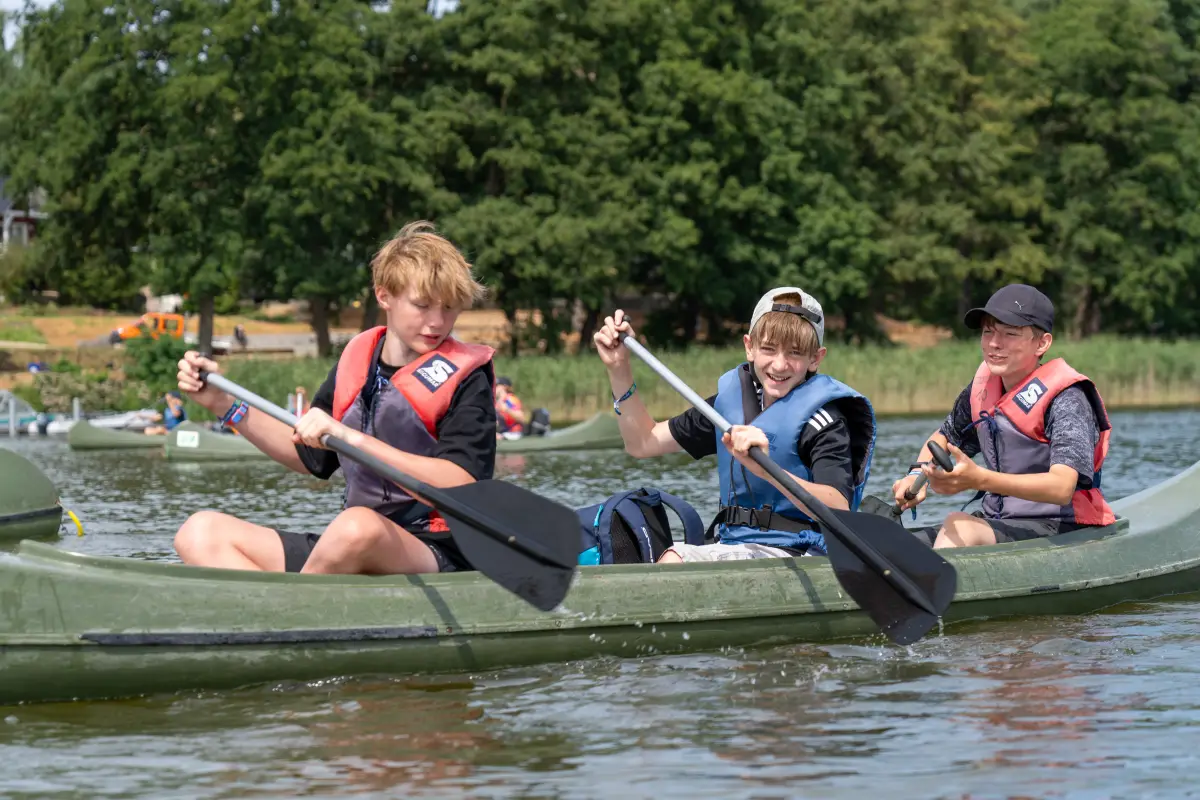 Three boys in life jackets paddling a canoe