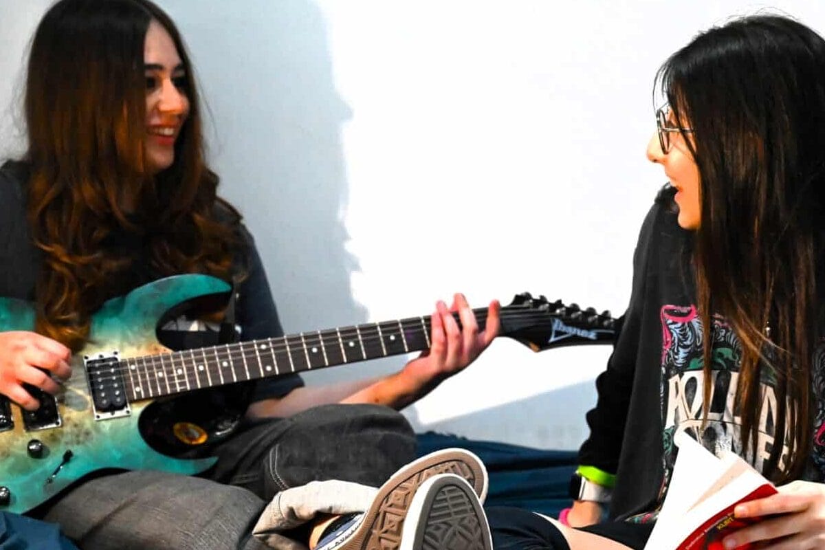 A student playing an electric guitar for a friend holding a notebook, in a Luckley House School boarding room