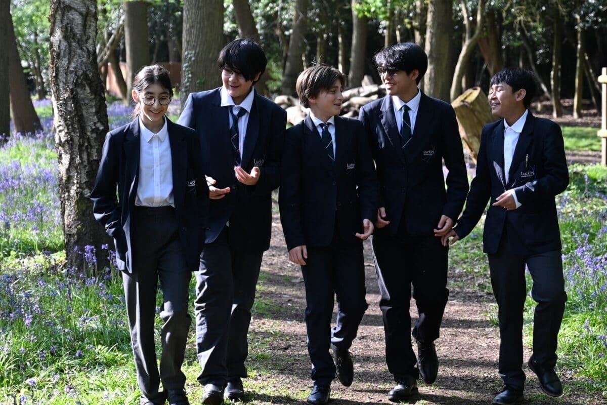 Five pupils in school uniform walking along a woodland path with bluebells on the Luckley House School campus