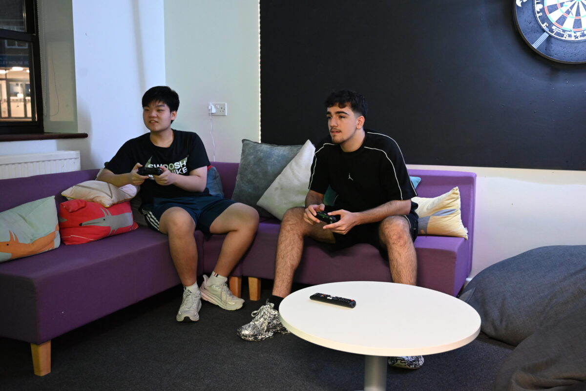 Two boys playing video games on the sofa in the Luckley House School common room, dartboard on the wall