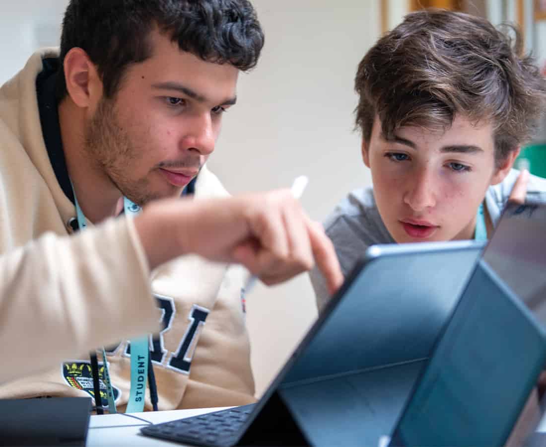 Two students leaning over a tablet together, one pointing at the screen, during a course session