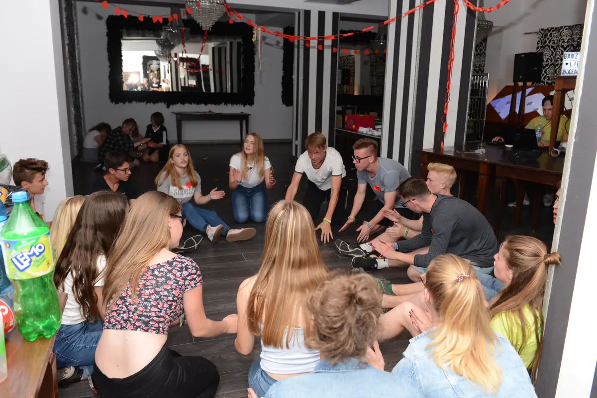 Teenagers sitting in a circle on the floor playing a group game indoors