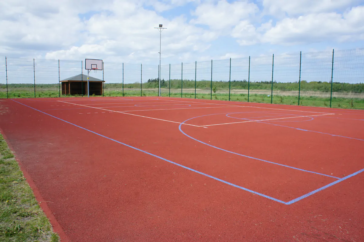 Fenced outdoor court with a red playing surface and a basketball hoop