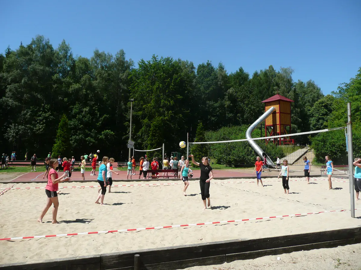 Children playing on the sand volleyball court of the holiday village, with trees behind