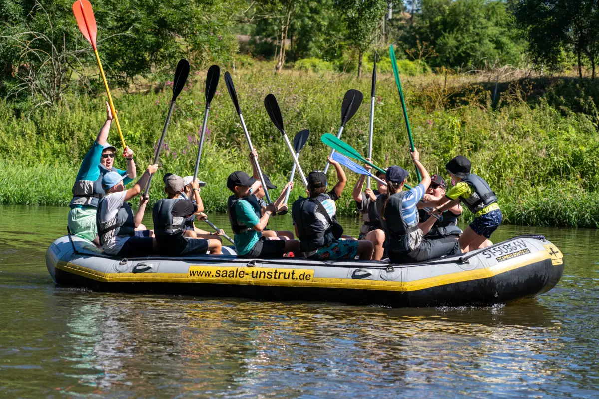 A group of campers in wetsuits paddling a large inflatable raft down the river