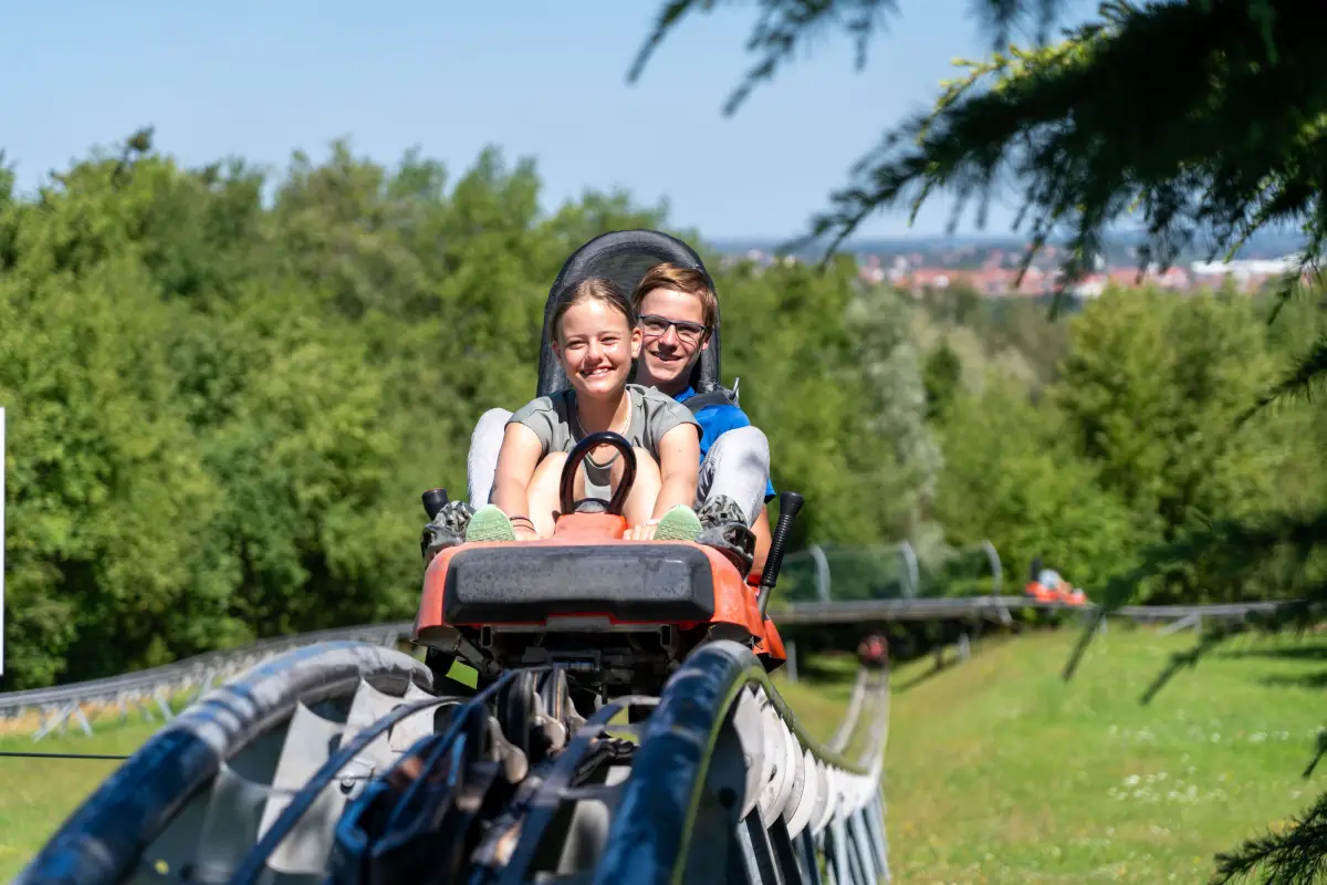 Two campers riding a cart down a summer toboggan run on an outing from the Aktivcamp