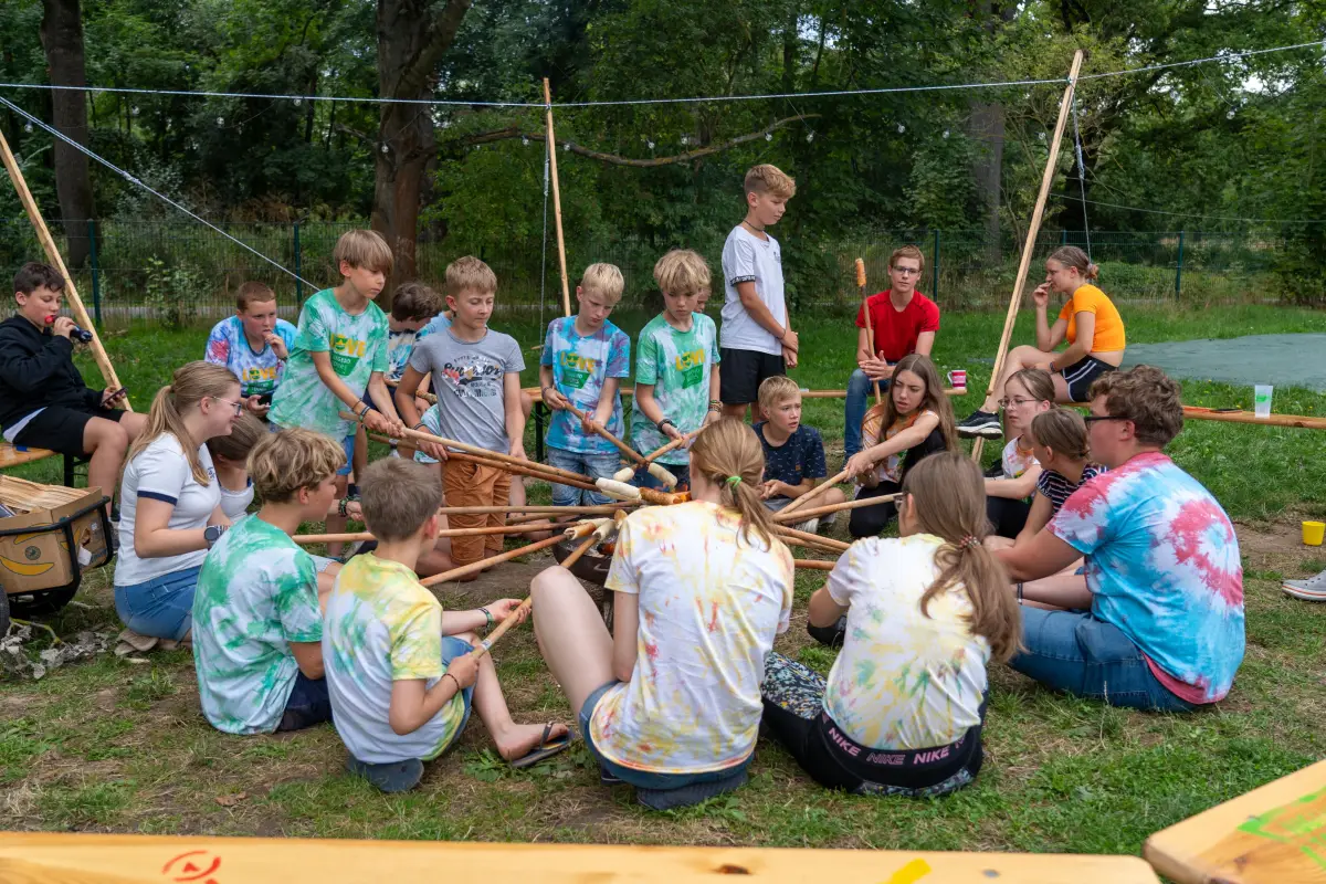 Campers sitting in a circle on the grass holding long poles during a group game