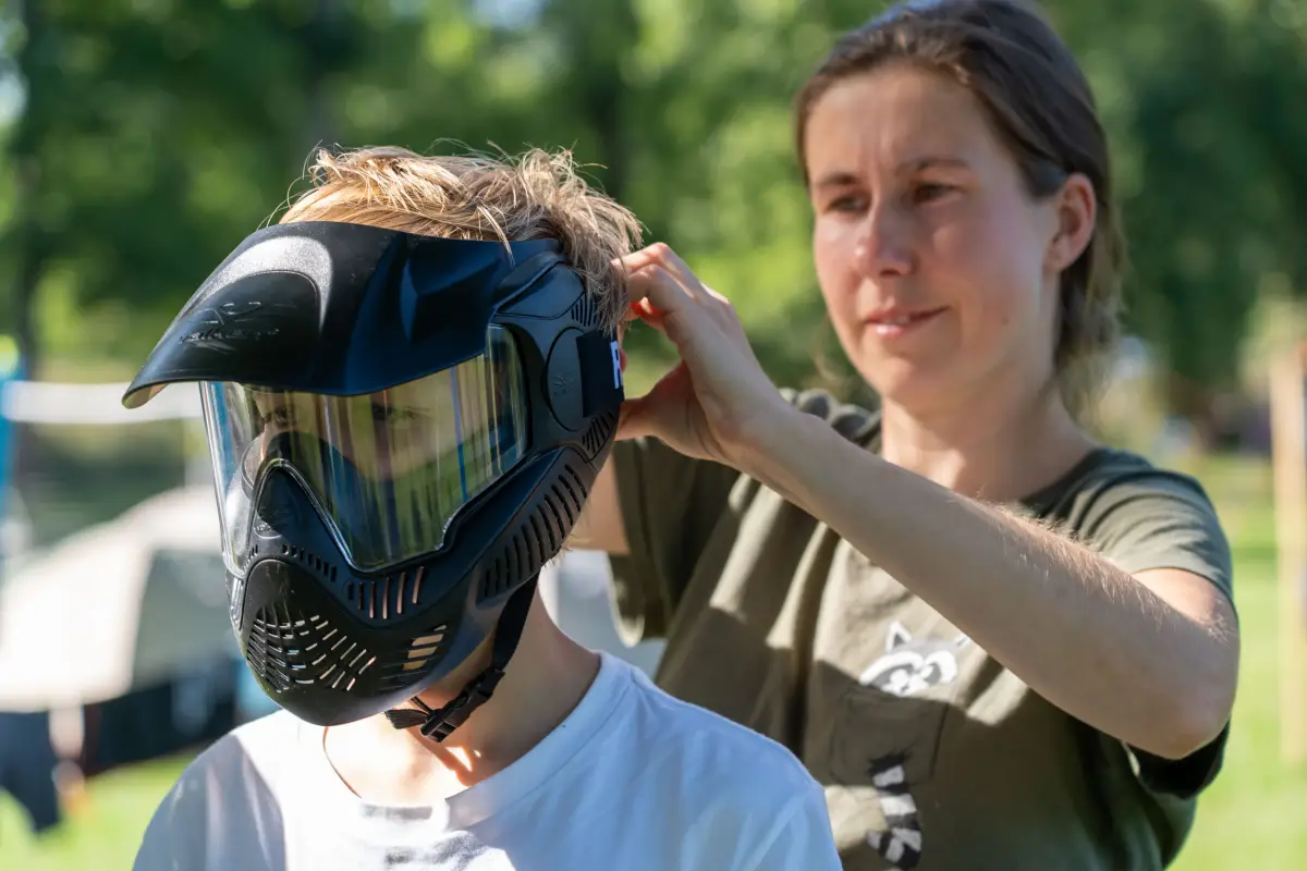 A camper holding up a mesh-fronted protective helmet used for the archery attack game