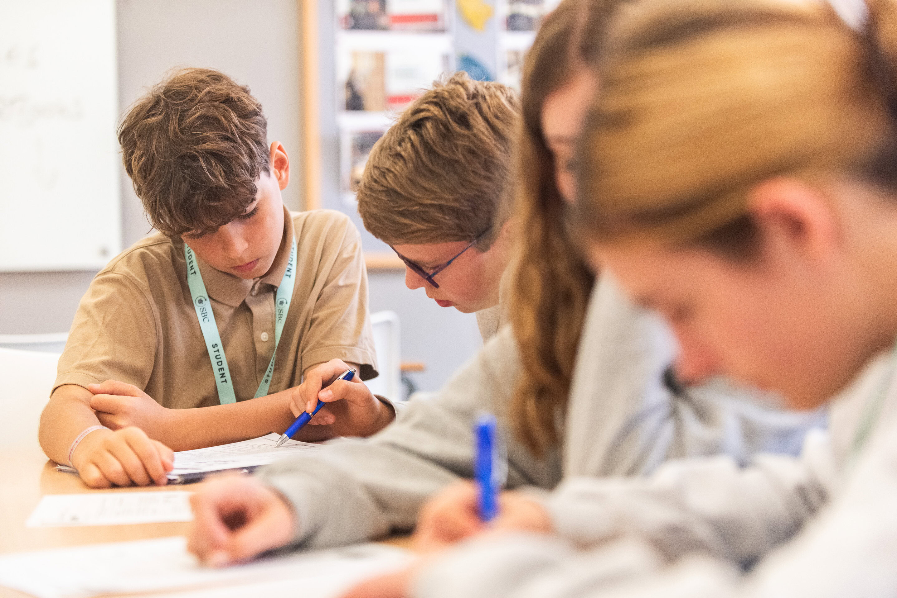Students write in workbooks with blue pens during a lesson at long desks