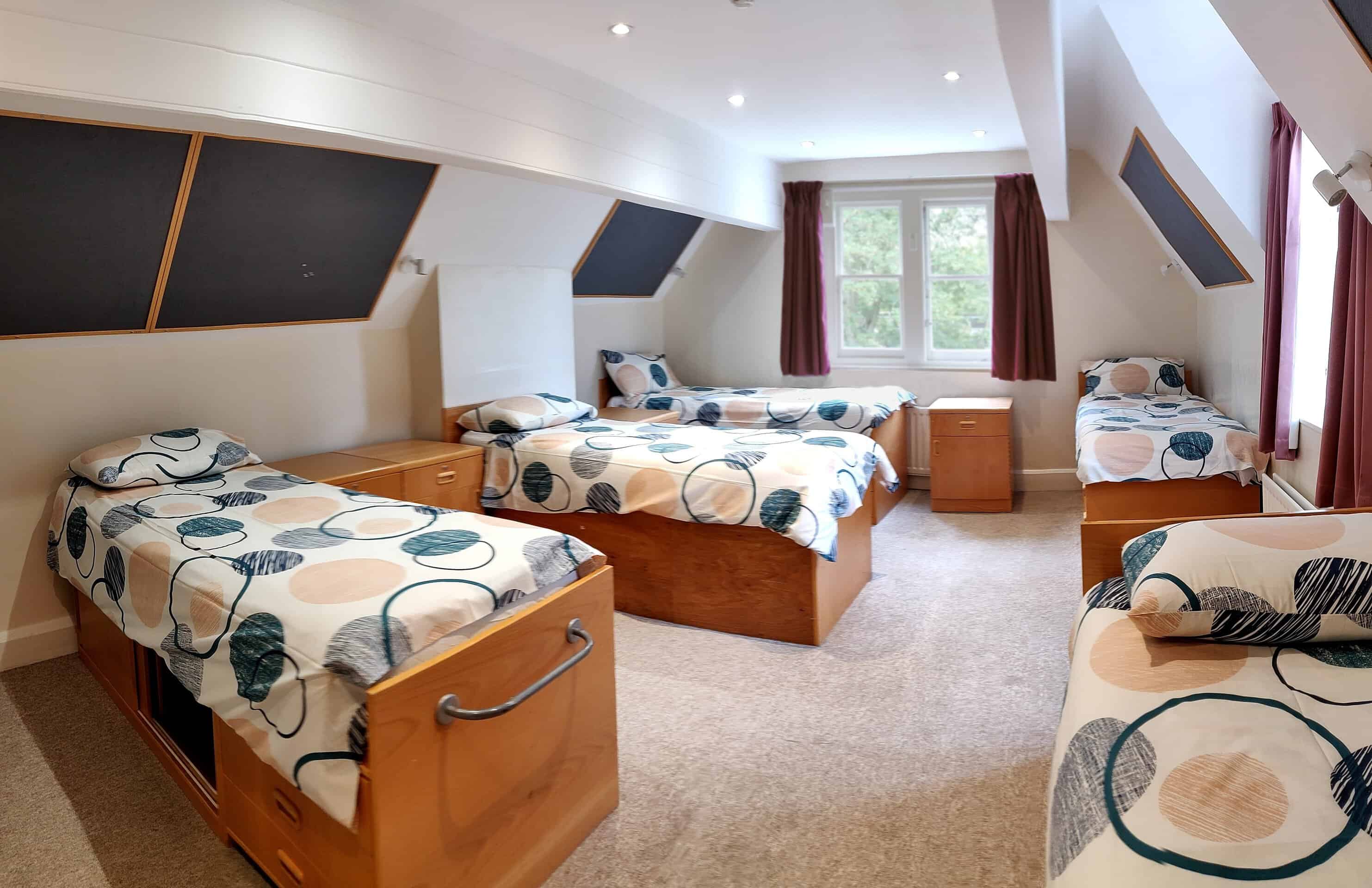 A boarding bedroom with three single beds and patterned covers under a sloping ceiling