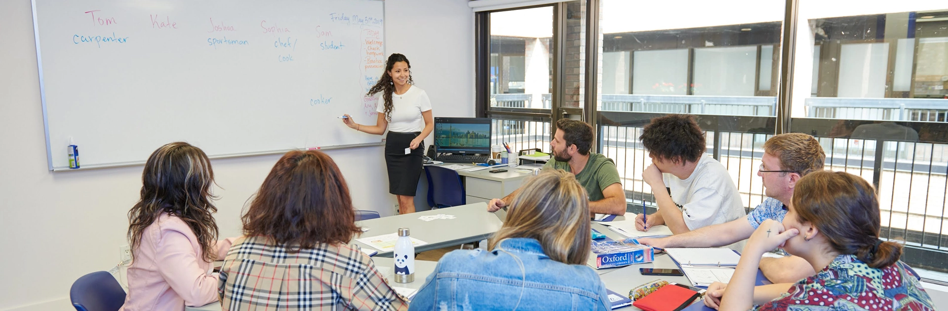A teacher writing on a whiteboard while students work at desks in a bright classroom at LSI Toronto.