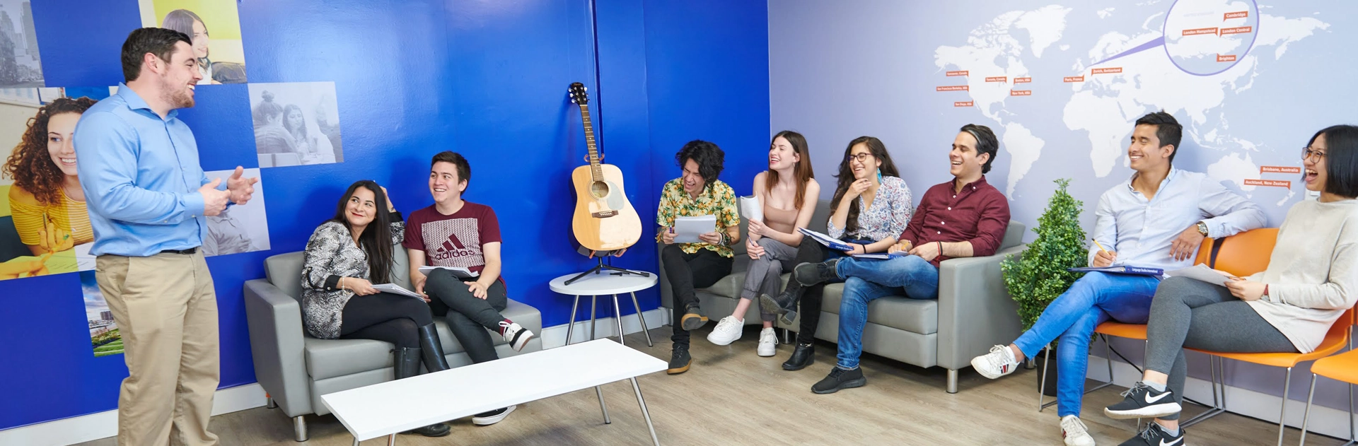 Students sitting on sofas and chairs in the LSI Toronto student lounge, a blue-walled room with a guitar against the wall.