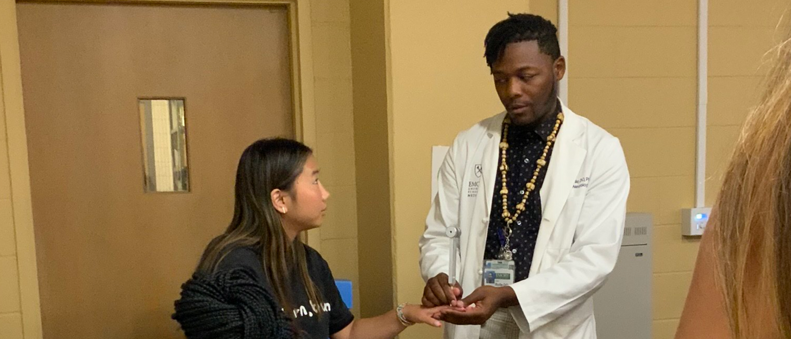 A medic in a white coat showing something held in his hand to a student, one to one, in a corridor of an Emory building