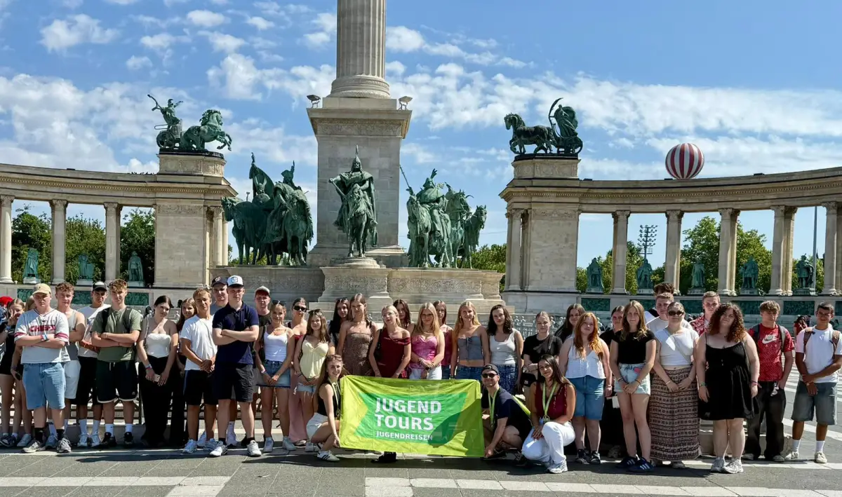 A large group of participants with a Jugendtours banner in front of the colonnade and statues on Heroes’ Square in Budapest