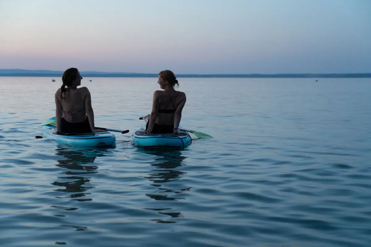 Two people paddling stand-up paddleboards on the calm water of the lake
