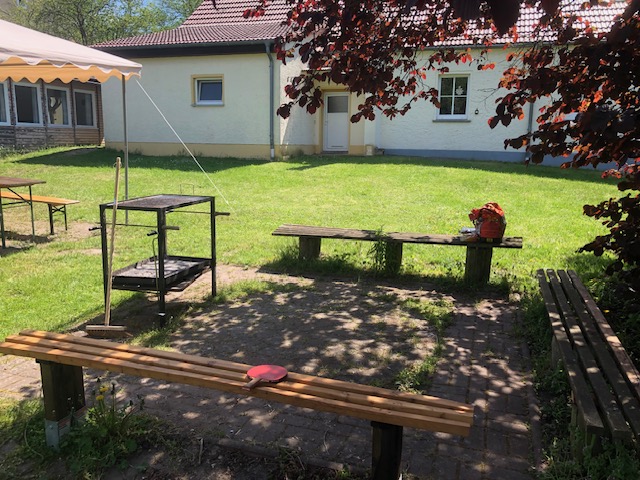 Paved courtyard with wooden benches and tables in front of a white single-storey building at the Rüstzeitheim Schorfheide in Vietmannsdorf