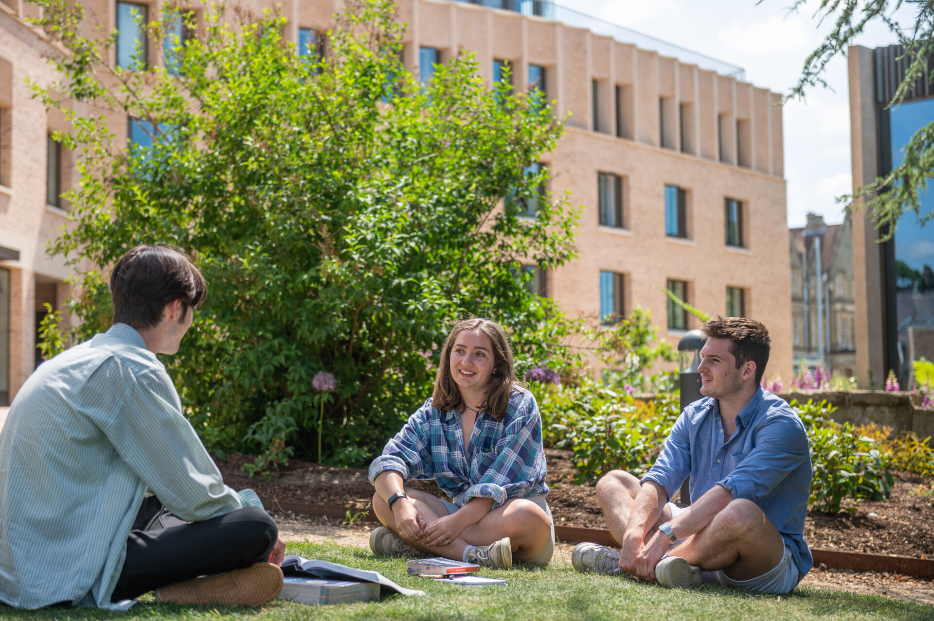 Students sitting on the grass in a garden in front of a brick college building at St Hilda's College, Oxford
