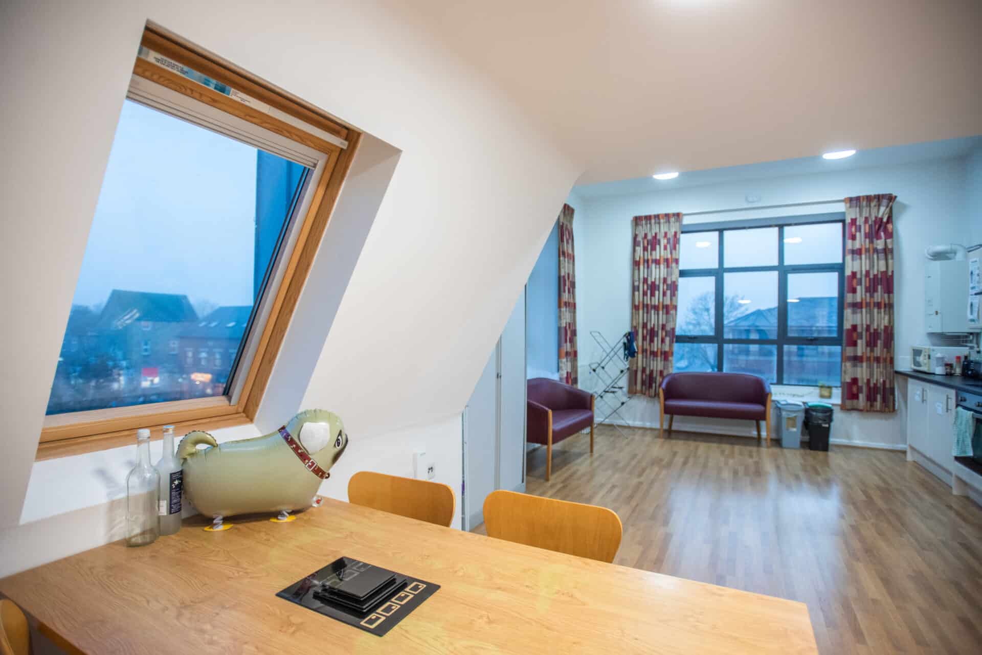 Student accommodation at St Hilda's College, Oxford, with a table, armchairs, kitchenette and large windows