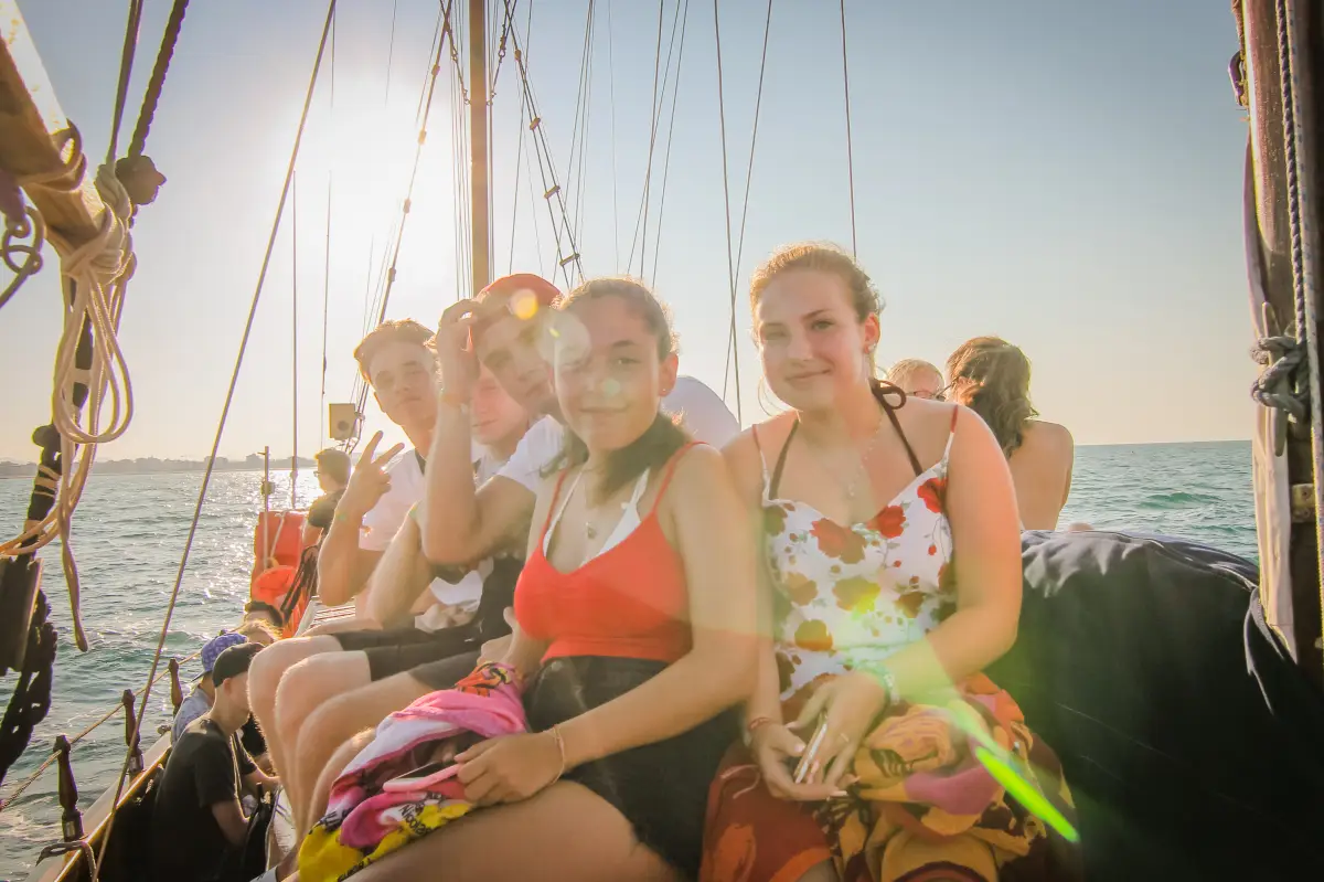 Group of teenagers sitting along the rail of a sailing boat at sunset on a Jugendtours excursion from Rimini