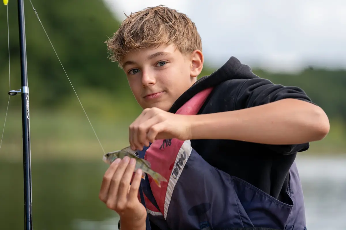 A camper by the water holding open a box of fishing lures and tackle