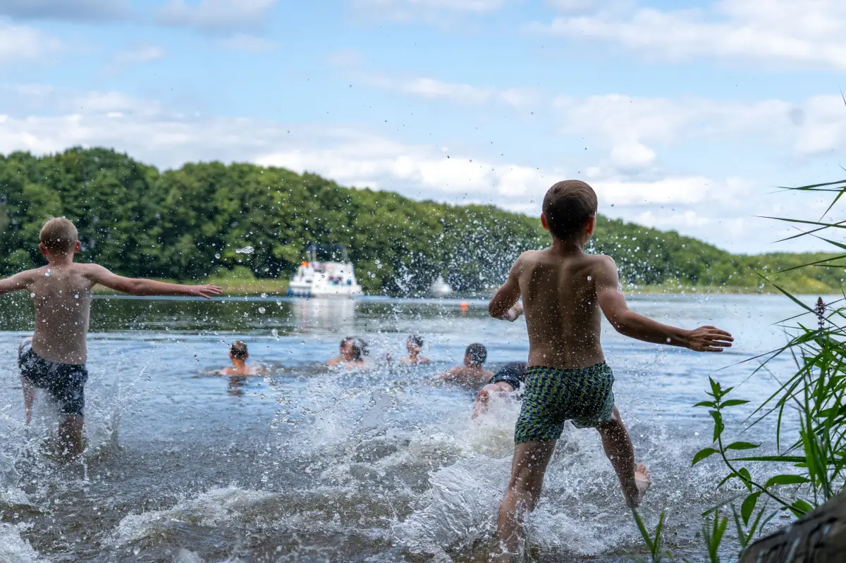 Campers splashing and swimming in the shallows of the lake with a motorboat moored behind