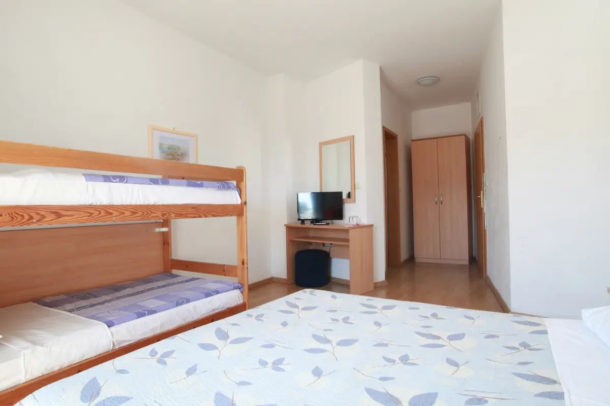 A hotel room with a bunk bed, a desk with a television and a wardrobe