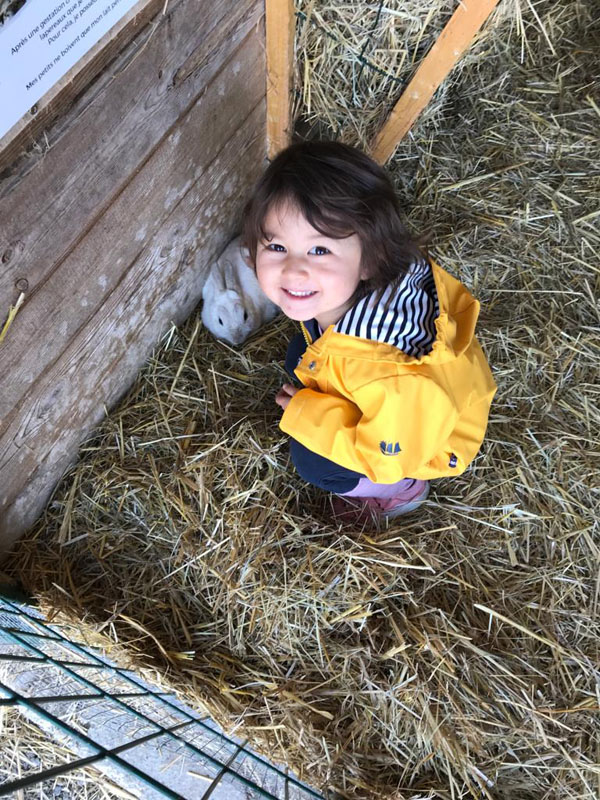A small child in a yellow raincoat crouching in the straw with a guinea pig at the teaching farm