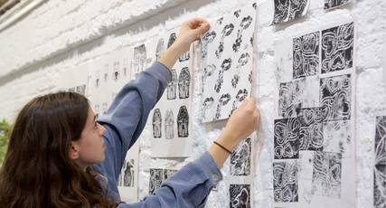 Student pinning black-and-white prints to a white brick wall, InvestIN Art & Design Summer Experience in London