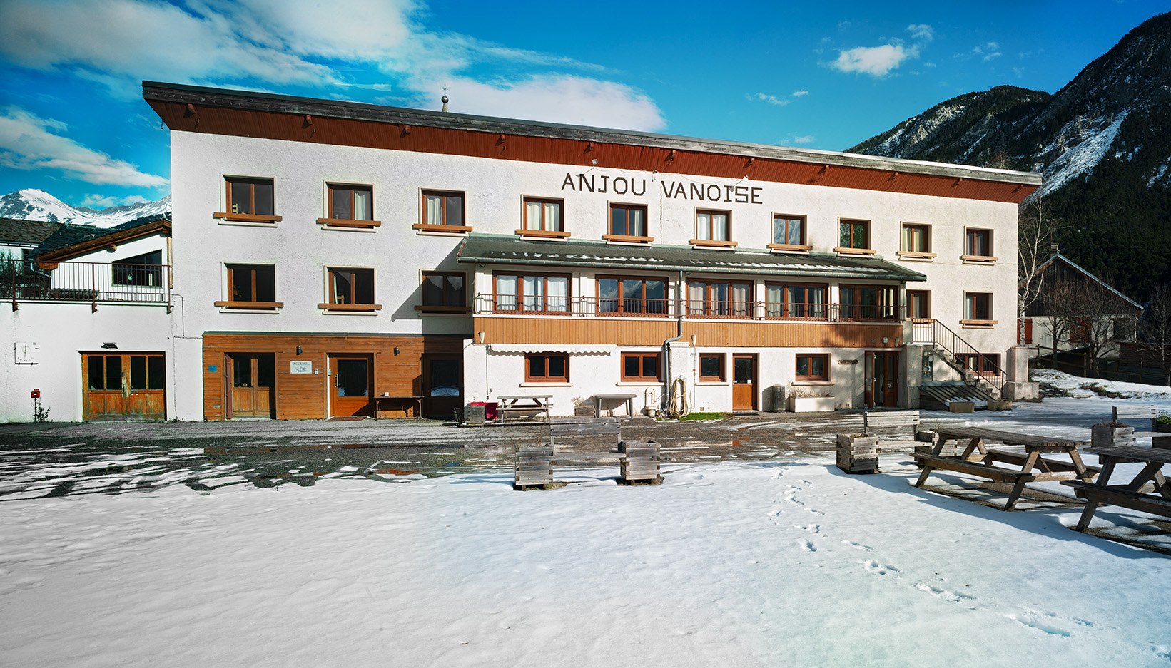 The Anjou Vanoise holiday centre building in Sollieres, Val Cenis, with snow in the yard and mountains behind