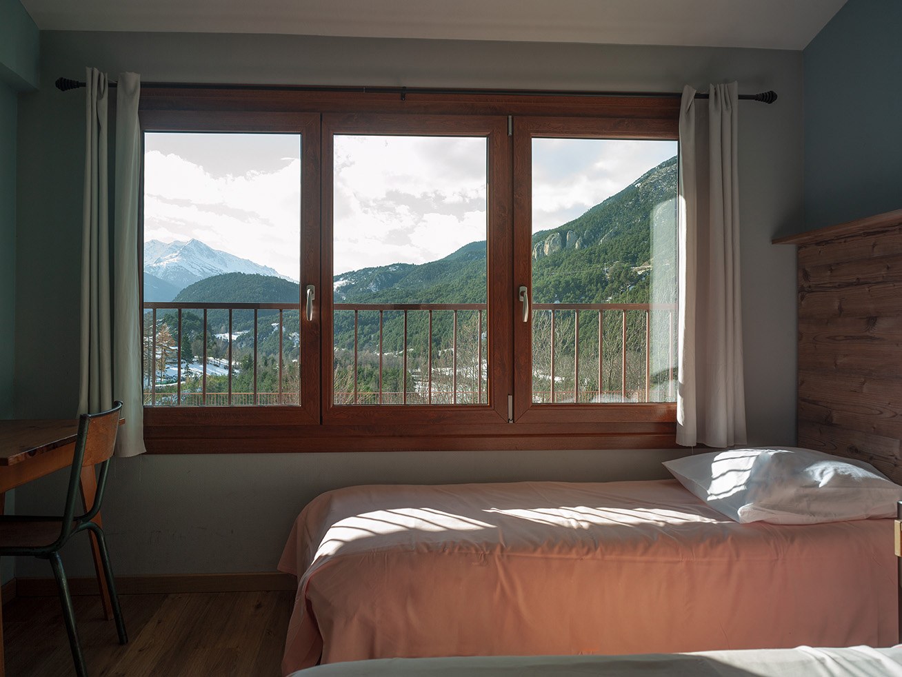 Bedroom at the Anjou Vanoise centre with a bed by a large window and balcony overlooking forested mountains